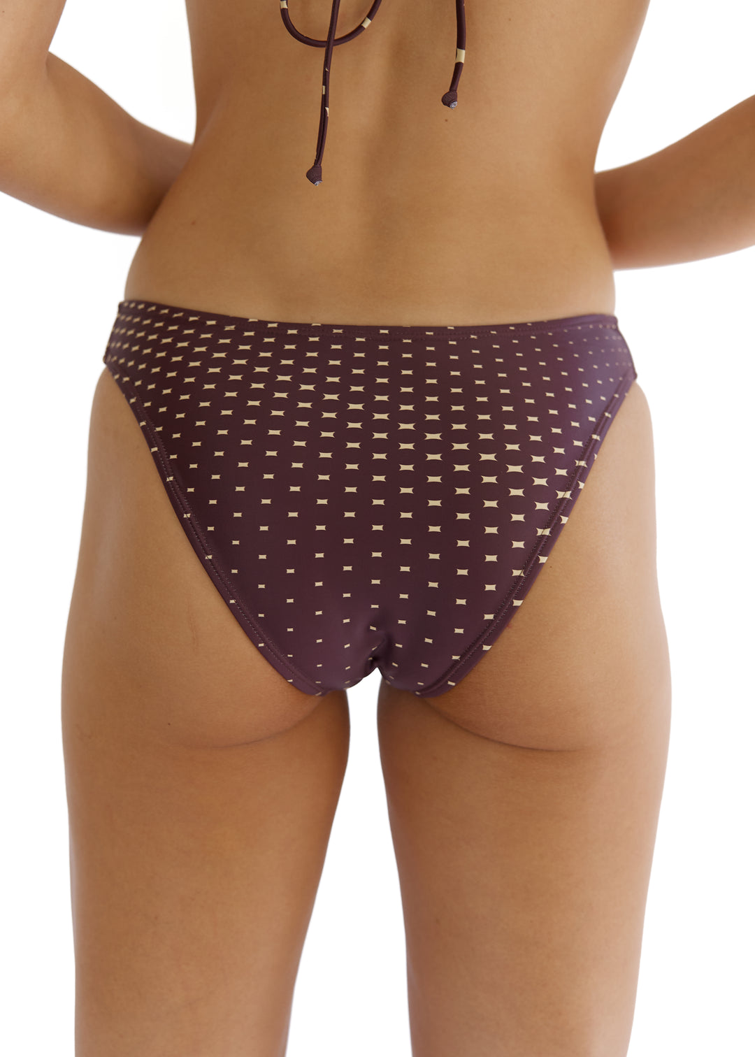 Back lower torso view of woman wearing a dark brown Isla Top with back ties and Isla Midi Bottoms with beige star pattern, mid-coverage on buttocks, elbows folded at sides on a white backdrop.