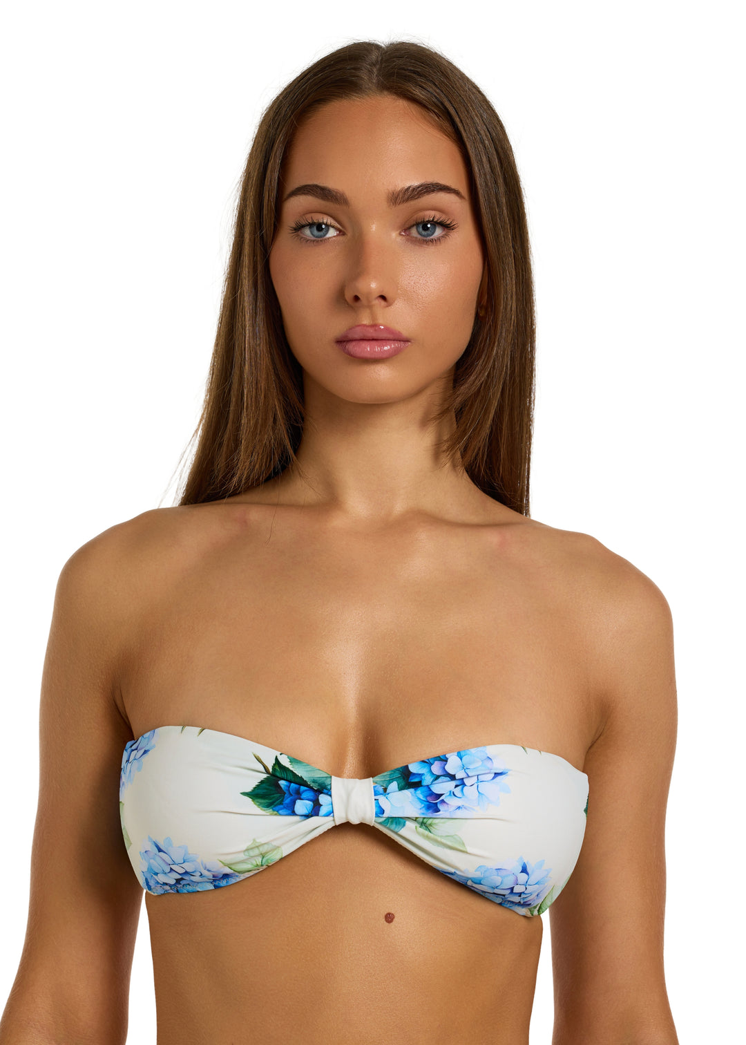 Woman with dark brown hair wearing a White Fleurs Duo Top in vibrant blue hydrangea floral print with green leaves, in bandeau top style and a gathered center, shown from head to upper midsection on a white backdrop.
