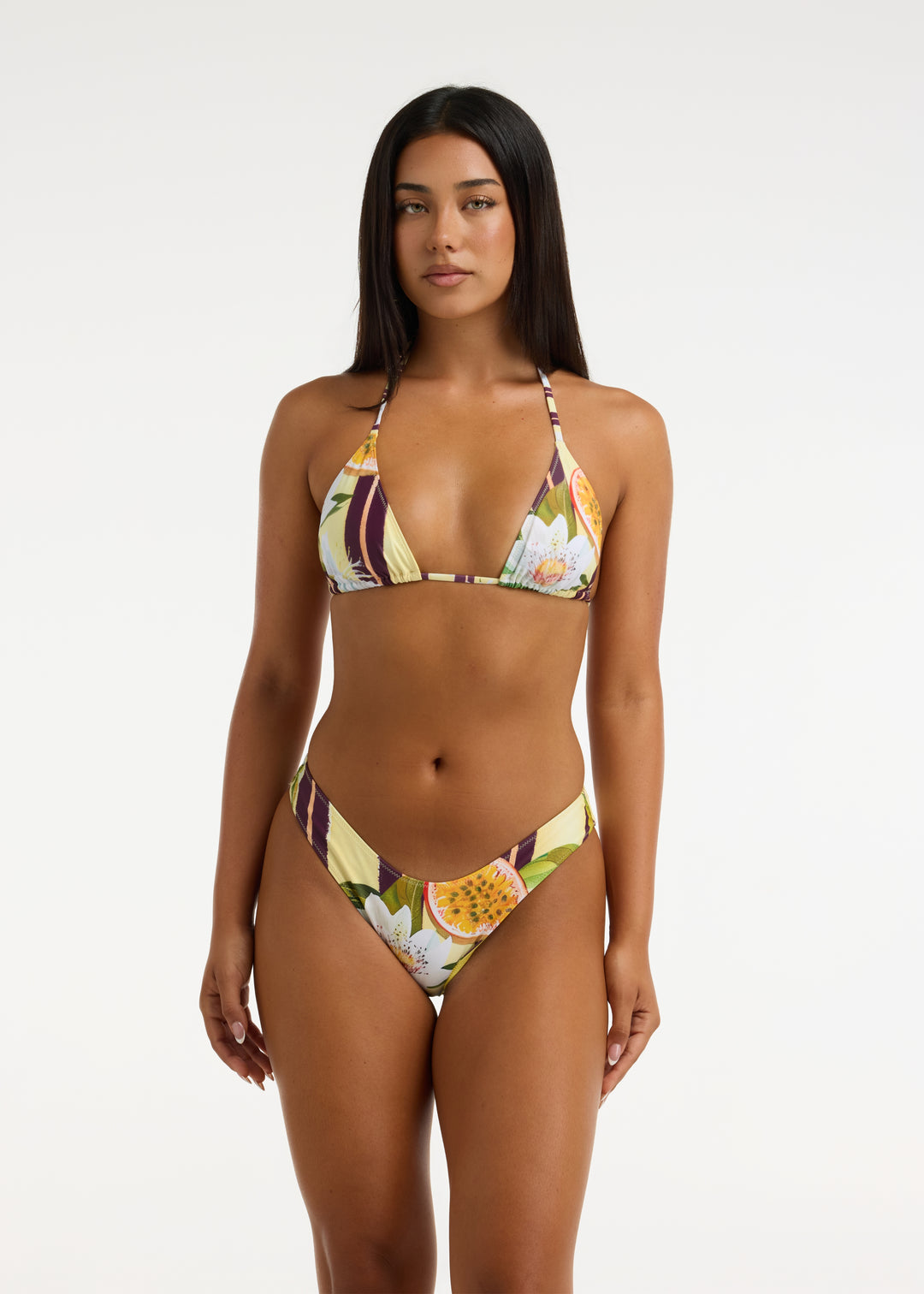 Model with long black hair wearing the Passiontini bikini top and Passiontini Midi Bottom in tropical passionfruit and floral print. The top features removable padding in a triangle halter shape and the bottoms are V shaped, mid coverage. With a thick waistband. Bottoms sit high-waisted on the model.