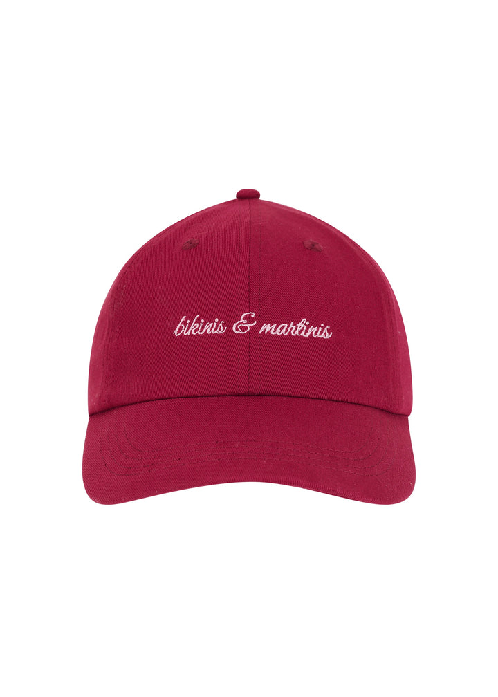Burgundy colored Martini cap with the words "bikinis & martinis" in soft pink cursive on the front, made from 100% cotton twill, classic baseball cap design, against a white backdrop.
