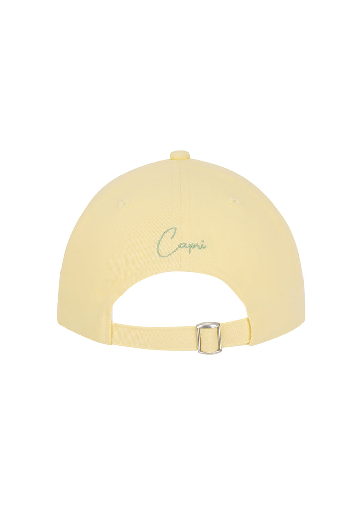 Light yellow Martini cap made from 100% cotton twill, classic baseball cap design, seen from the back, featuring the word "Capri" in silver cursive. Adjustable strap with a silver buckle, against a white backdrop.